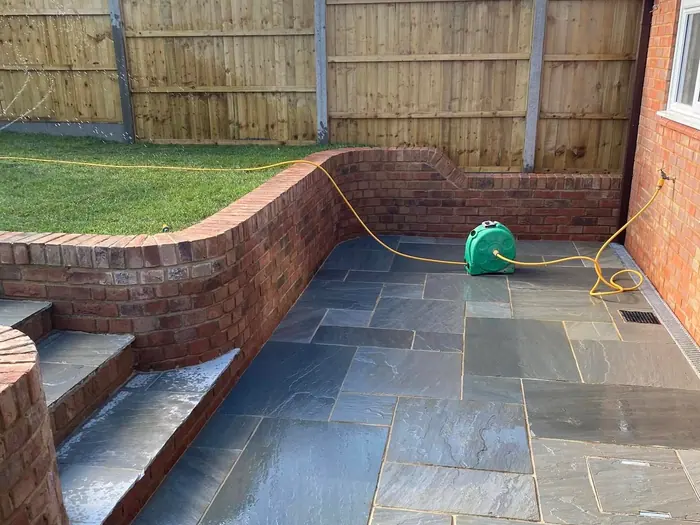 A curved brick retaining wall and slate patio in a landscaped, sloping garden